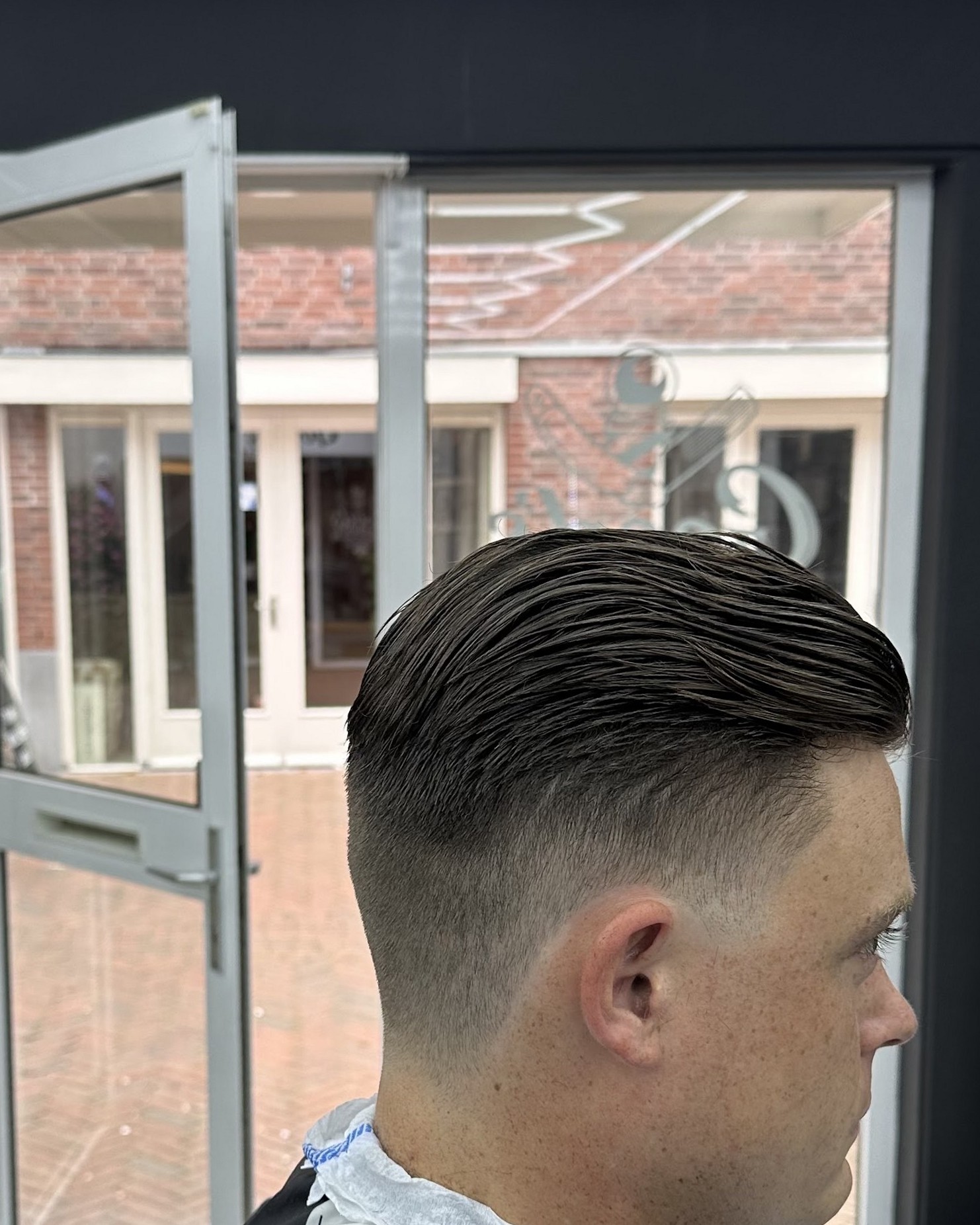 Een fade met een scheiding, net geknipt, in de stoel bij de open deur van de zaak